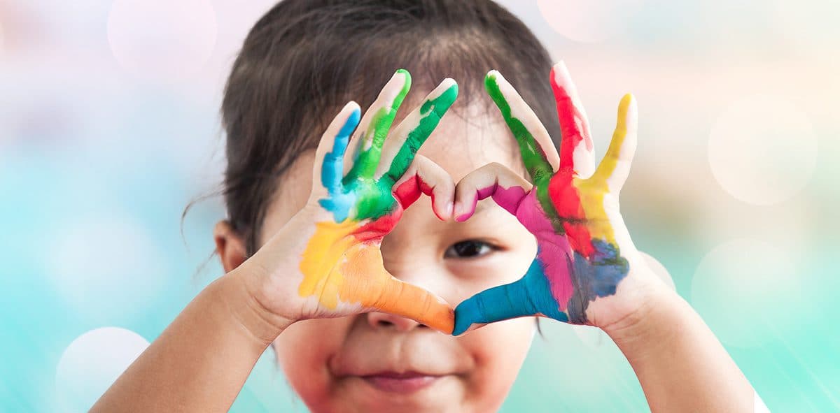 A preschool child making a heart with painted hands